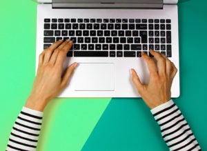 Woman hands typing on laptop computer on colorful background.