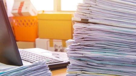 documents on desk stack up high waiting to be managed.