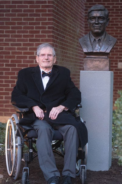 Robert Carey in wheelchair next to bronze bust