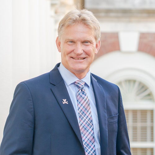 headshot portrait of Dr. Chris Holstege wearing a blue suit jacket with blue shirt and plaid tie